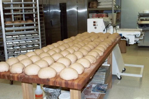 Trays of shaped buns rising on a wooden bench in the bakery